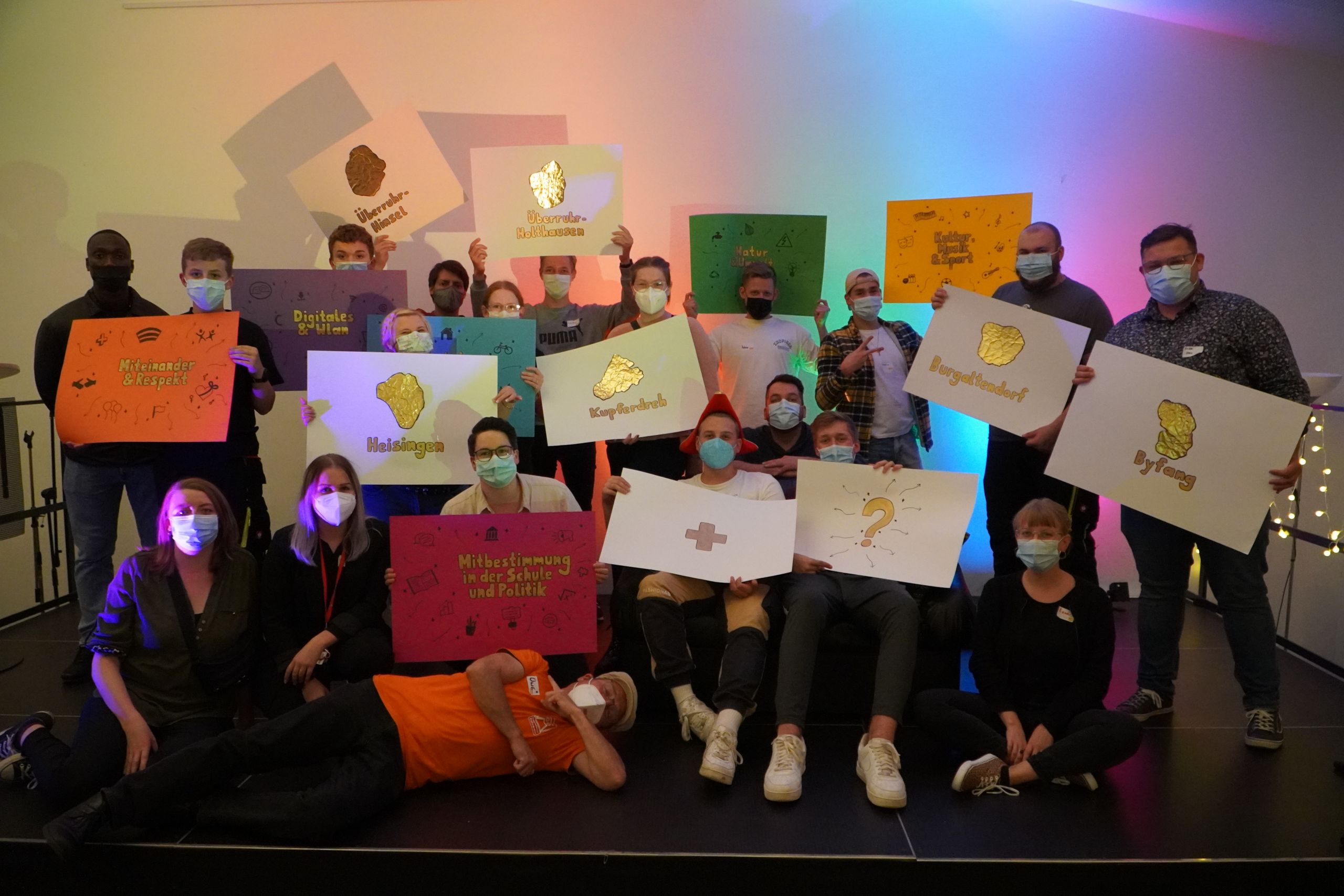 Eine Gruppe Jugendlicher steht zusammen für ein Gruppenfoto. Sie halten Schilder mit Ideen für Jugendbteiligung in ihrem Stadtteil hoch.